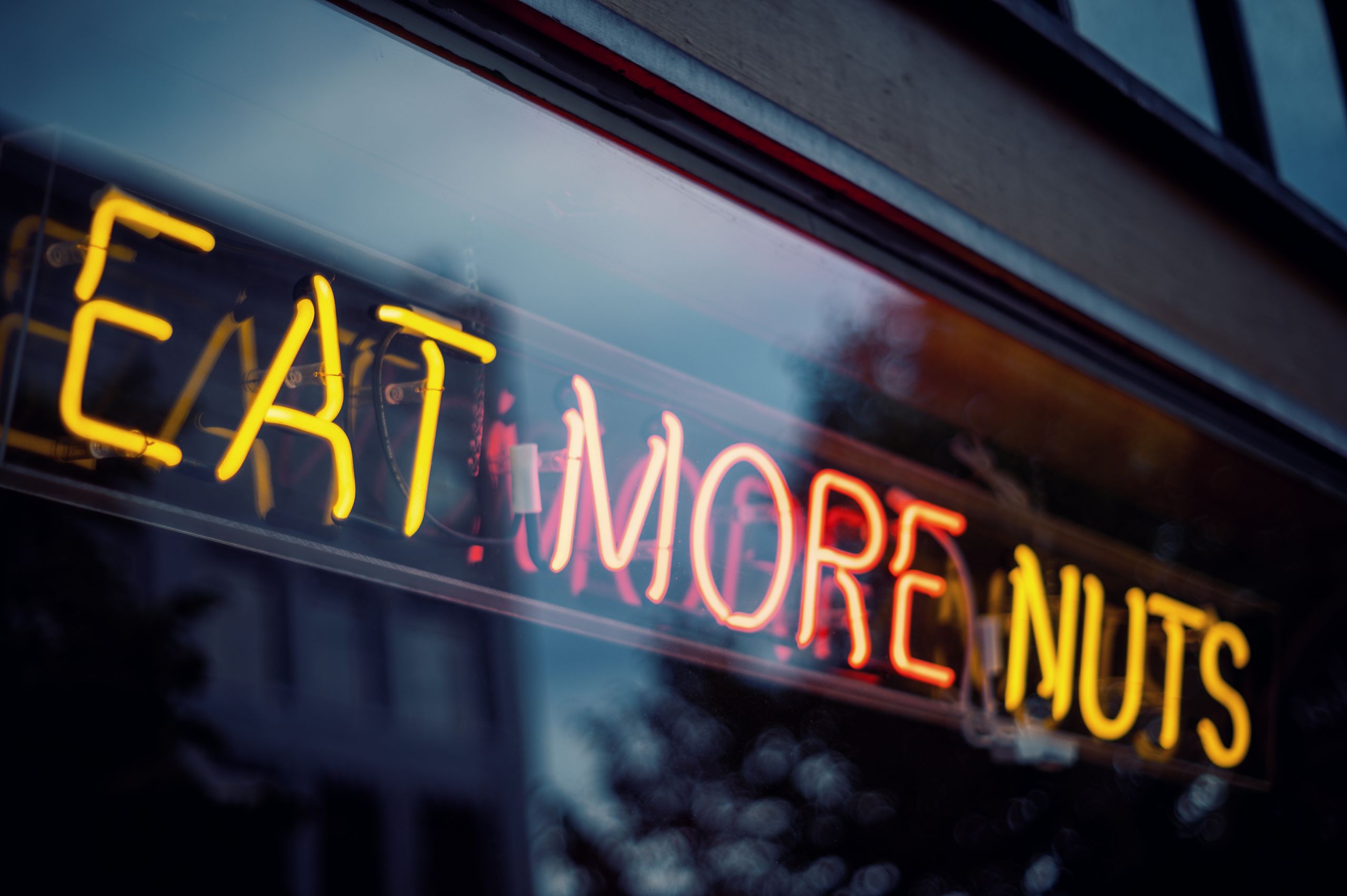 Bright neon sign with text 'Eat More Nuts' displayed on a storefront window.